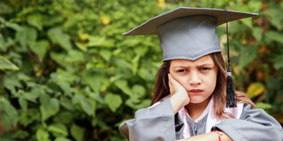Ein ca. 10 Jahre altes weiblich gelesenes Kind im Talar guckt unzufrieden und stützt den Kopf in die Hand